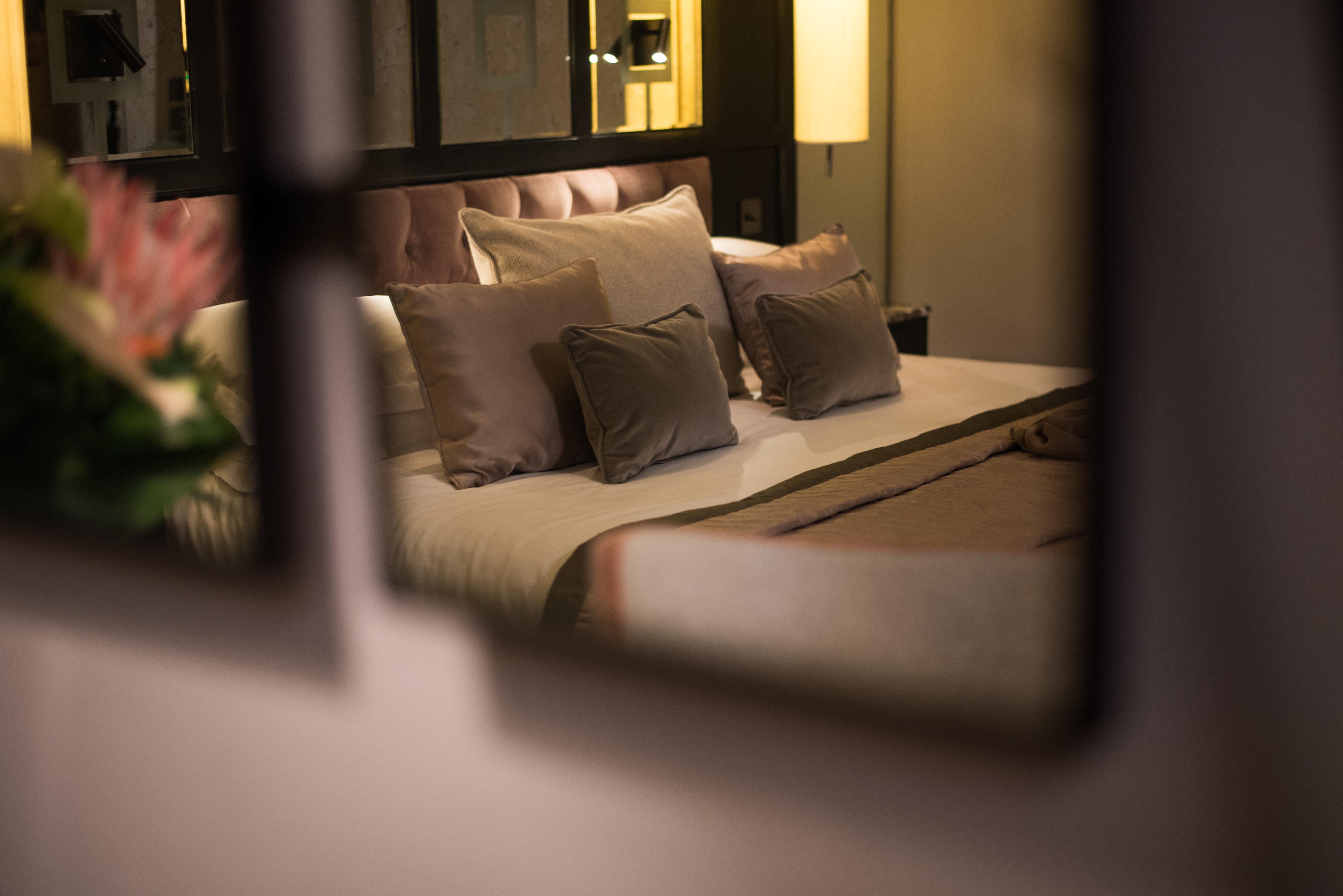 The Fitzwilliam Hotel Belfast Dış mekan fotoğraf The photo shows a cozy and elegantly decorated bedroom. The focal point is a plush bed with soft, neutral-colored bedding and several decorative pillows arranged neatly on it. The room has a warm ambiance, enhanced by a standing lamp that provides so