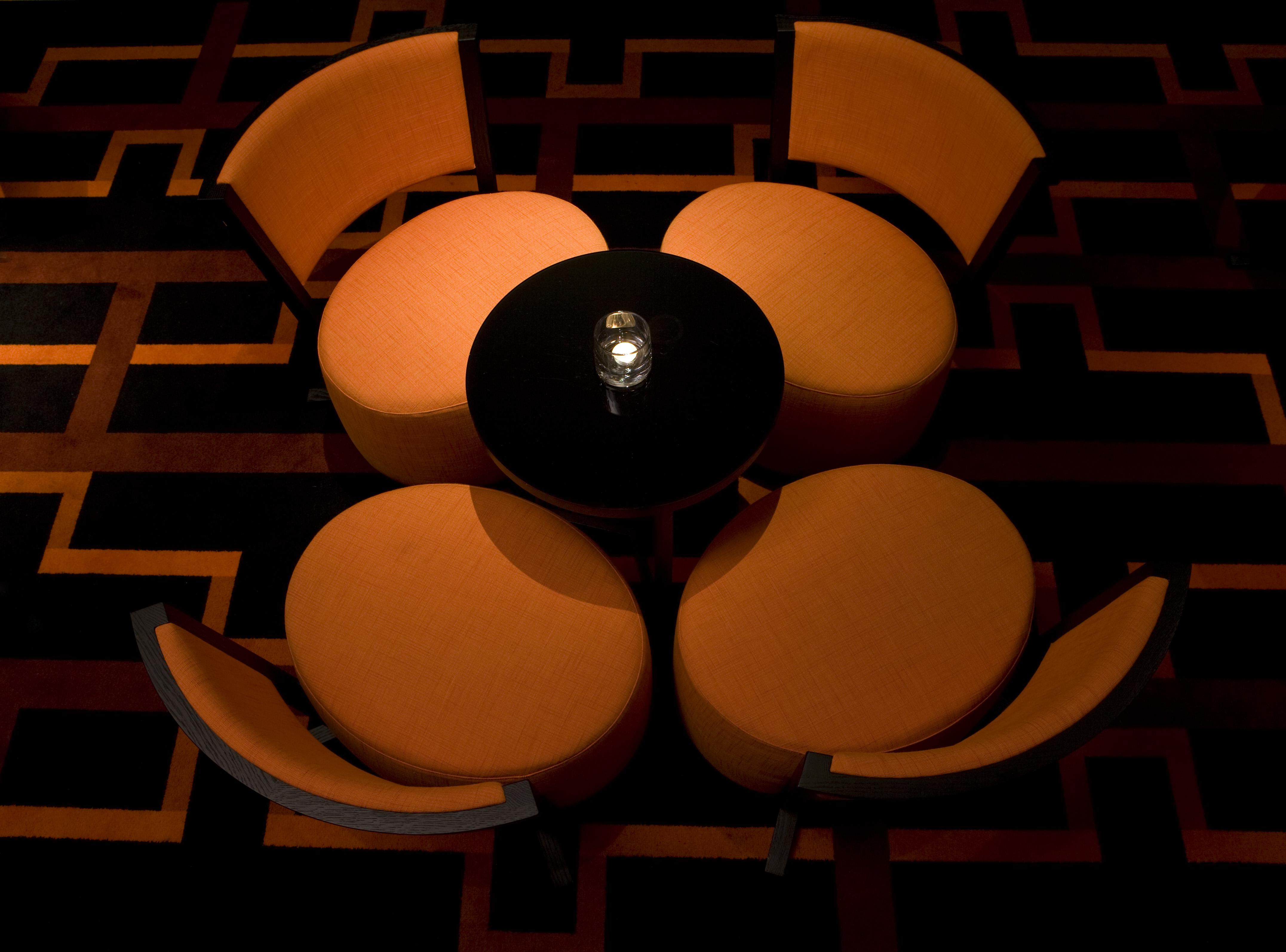 The Fitzwilliam Hotel Belfast Dış mekan fotoğraf The image shows a small seating arrangement consisting of four orange chairs arranged around a circular black table. The setting appears to be in a dimly lit area, emphasizing the warm tones of the chairs and the dark finish of the table. The floor d